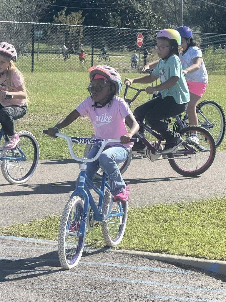 Students ride bicycles on a sidewalk.
