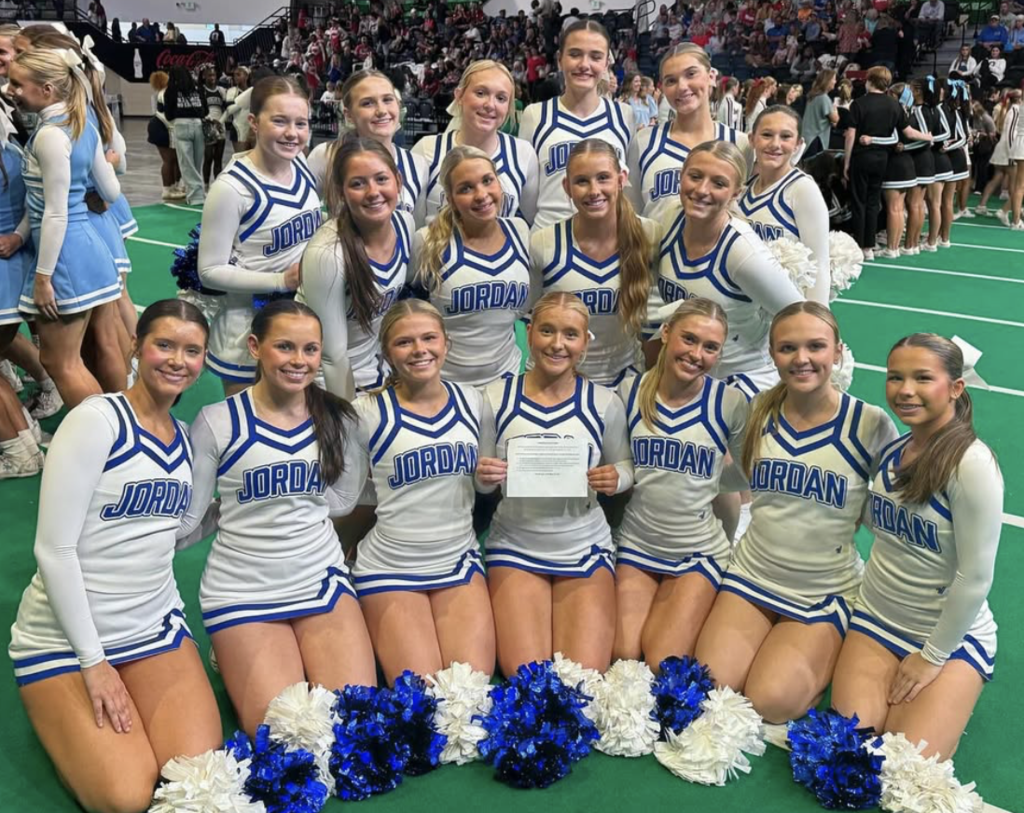 Mortimer Jordan High School cheerleaders stand and sit together for a photo. They're on a green mat.