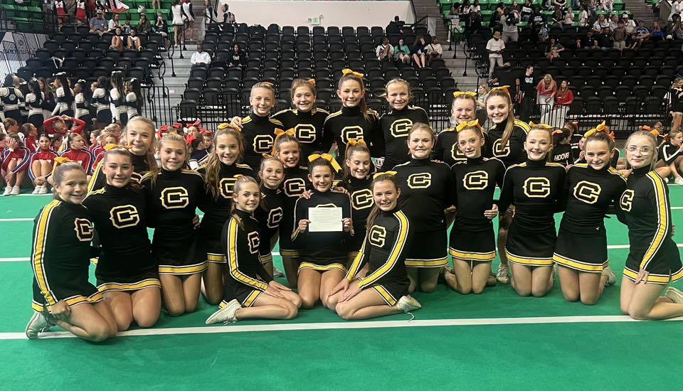 Corner Middle School cheerleaders pose together for a photo on a green cheer mat inside an arena.