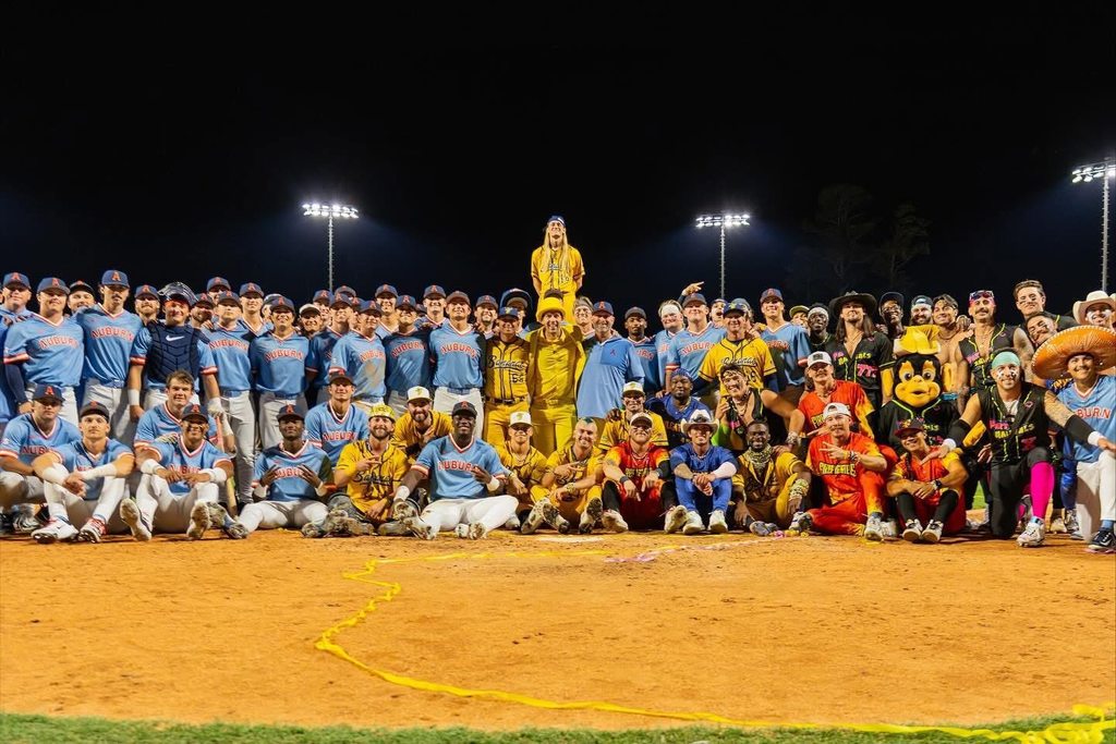 The Savannah Bananas and Auburn Baseball team stand and sit together for a photo on a baseball field.