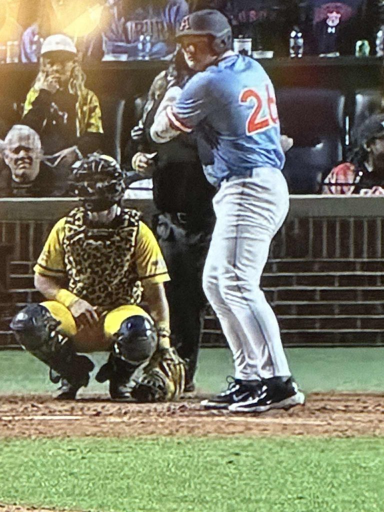 The photo is of a batter, catcher and umpire at home plate. The batter is getting ready for the pitch to be thrown.