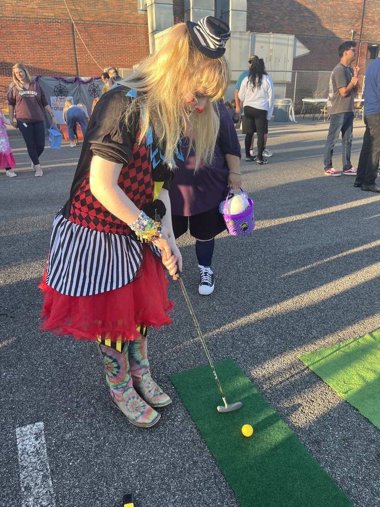 A person in a halloween costume plays put-put while attending a halloween party in a parking lot.