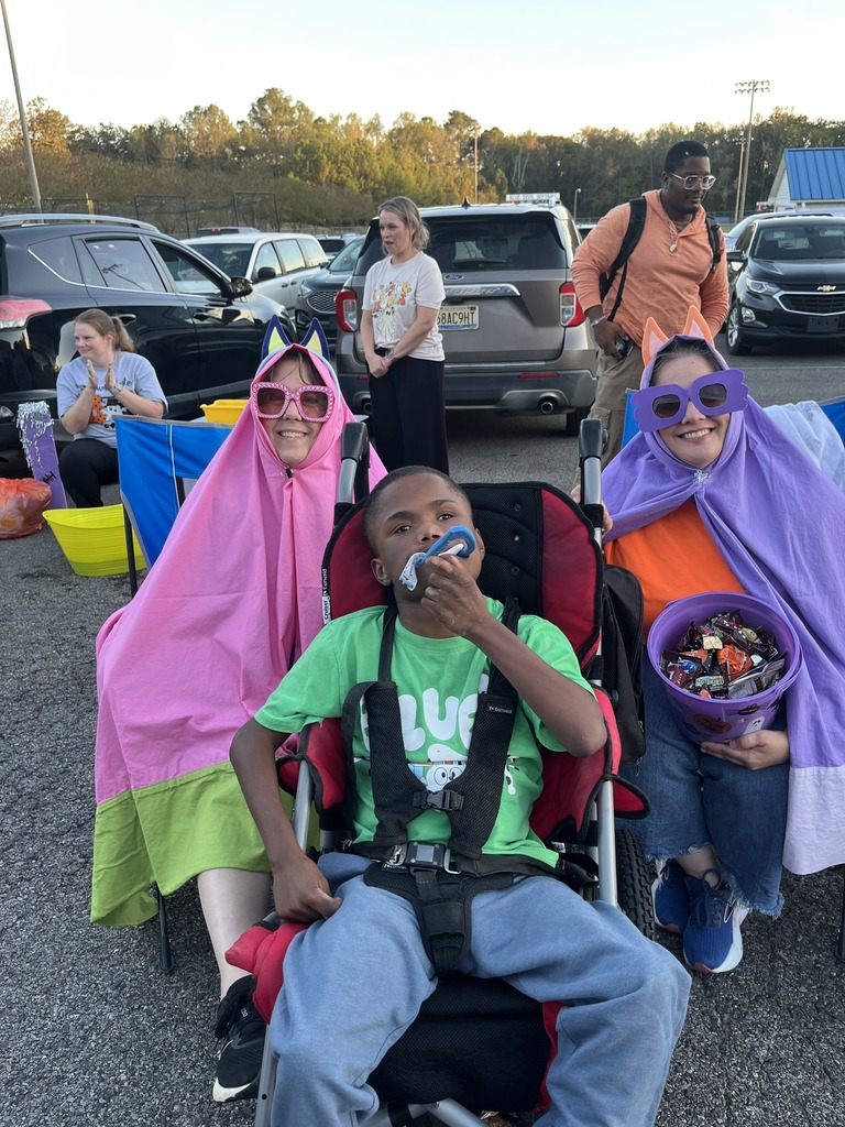 A student and adults pose for a picture while attending a halloween party in a parking lot. The adults are wearing costumes.