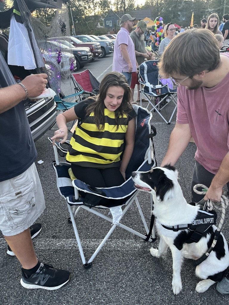 The photo shows a girl in a bumble bee costume smiling at an emotional support dog while the dog's owner holds the dog's leash. They sit and stand in a parking lot.