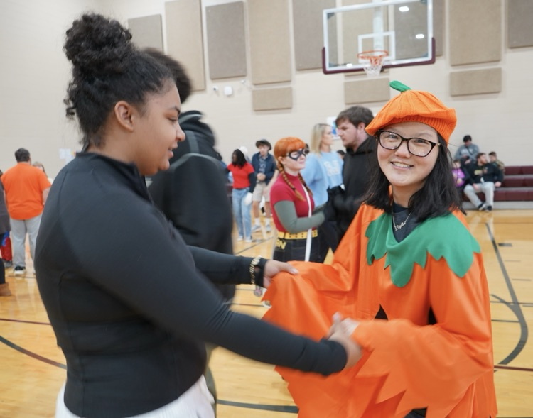 Two students dance together in a school gym. One is wearing a pumpkin costume  