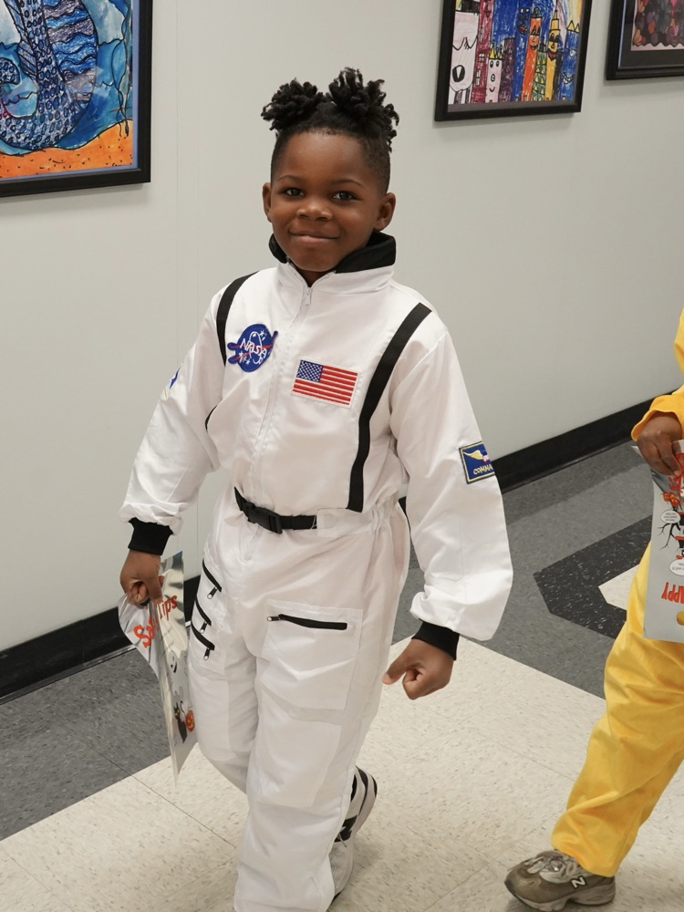A child walks in a school hallway while wearing an astronaut costume.