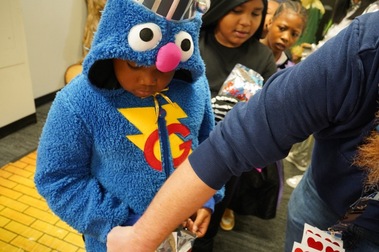 A student in a “Super Grover” costume trick-or-treats in a hallway.