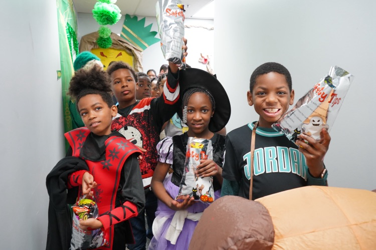 Students smile while holding up candy in a hallway.