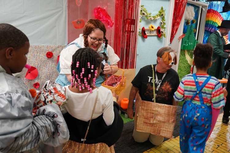An adult dressed as “Dorothy” from the Wizard of Oz and a man dressed as Toto hand out candy to students