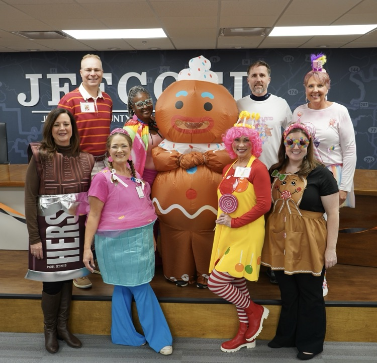 Board employees wearing candyland themed costumes stand together and smile.