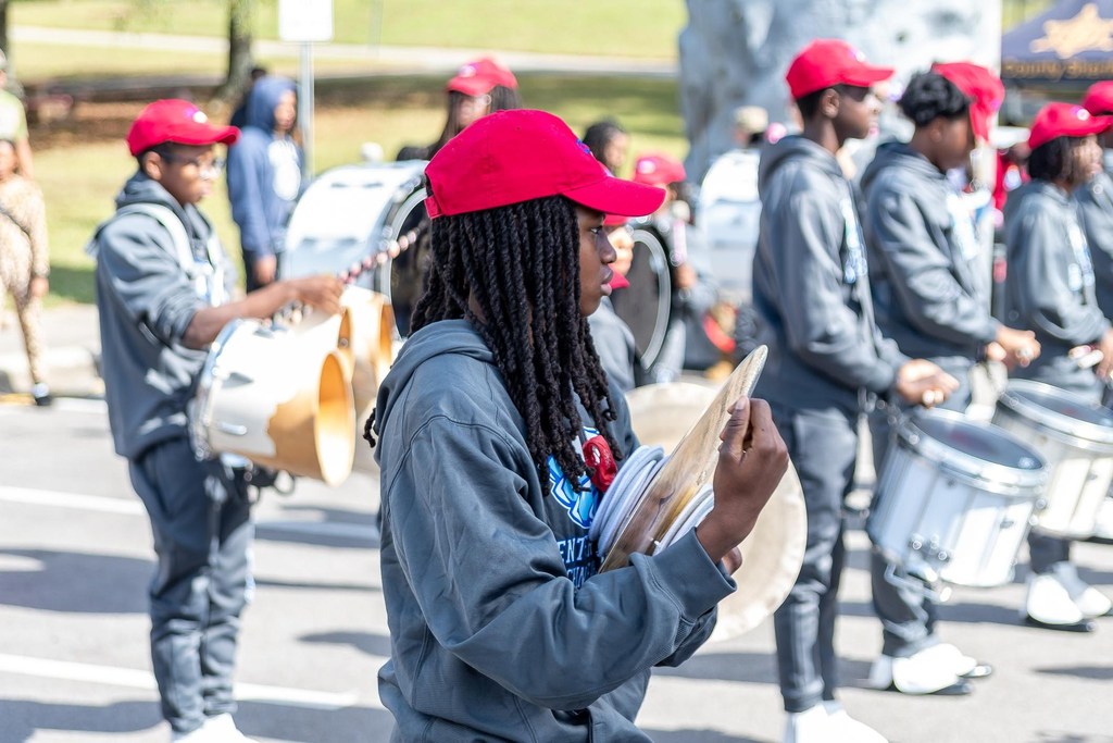 Center Point High School's marching band performs in a parking lot. In this photo, students are playing symbols and drums. They're wearing matching gray sweatsuits and red hats. 