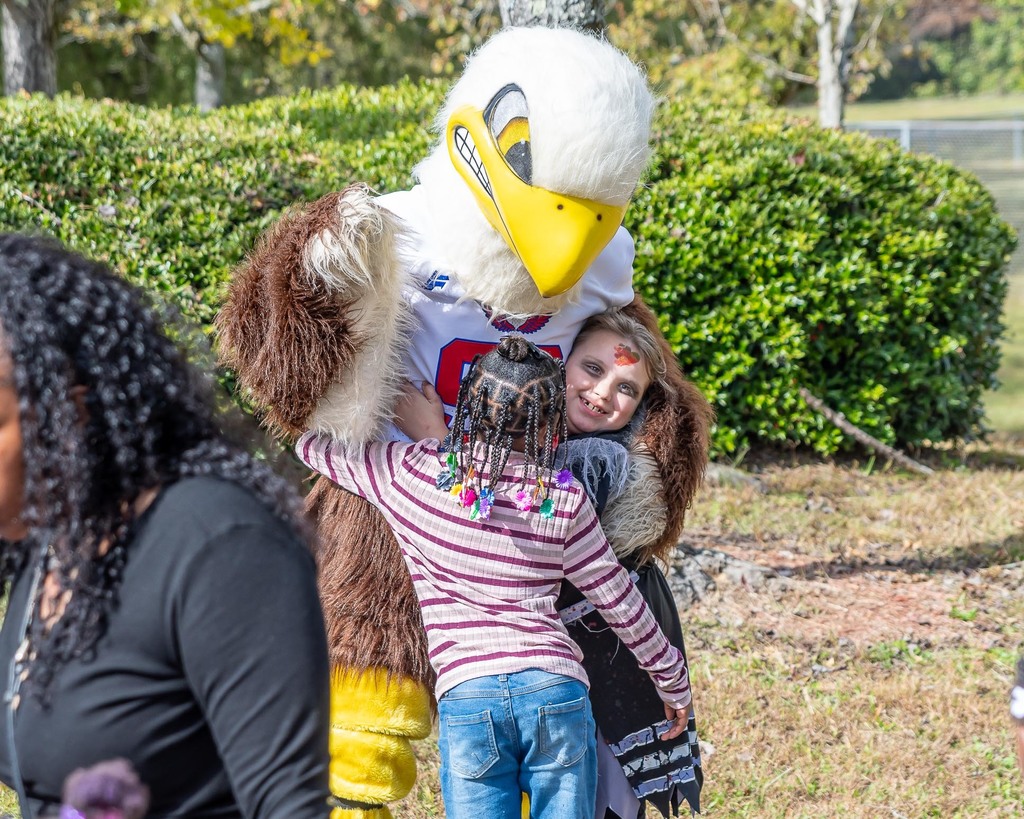 Two little girls hug an eagle mascot.