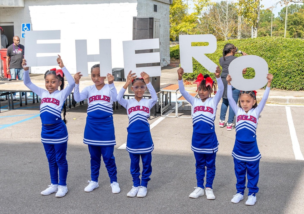 Little Eaglettes cheerleaders hold up letters that spell out EHERO while performing in a parking lot.