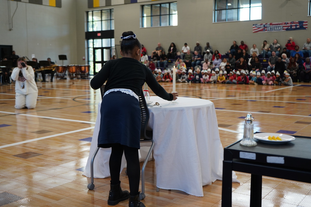 A child places a candle onto a table inside a school gym.