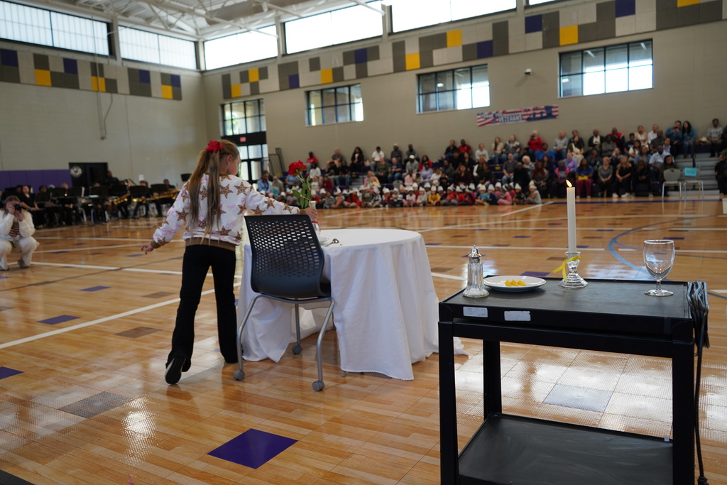 A girl places a vase onto a table inside a school gym.
