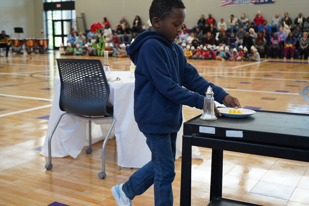 A child picks up a plate from a table inside a school gym.