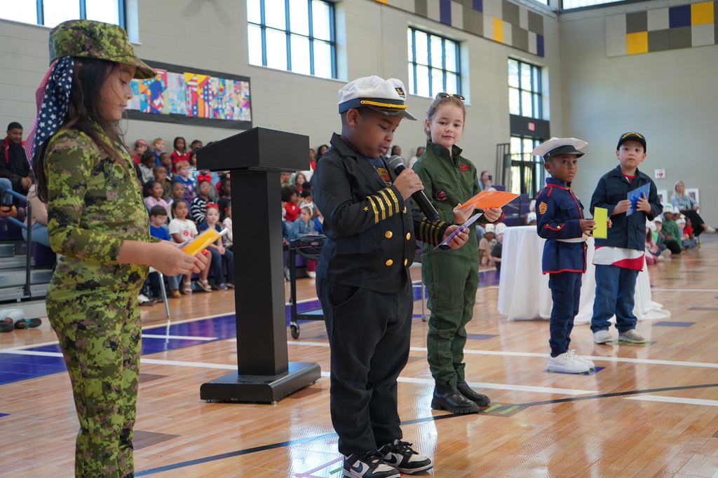Students wearing U.S. military uniforms give a presentation in a school gym.
