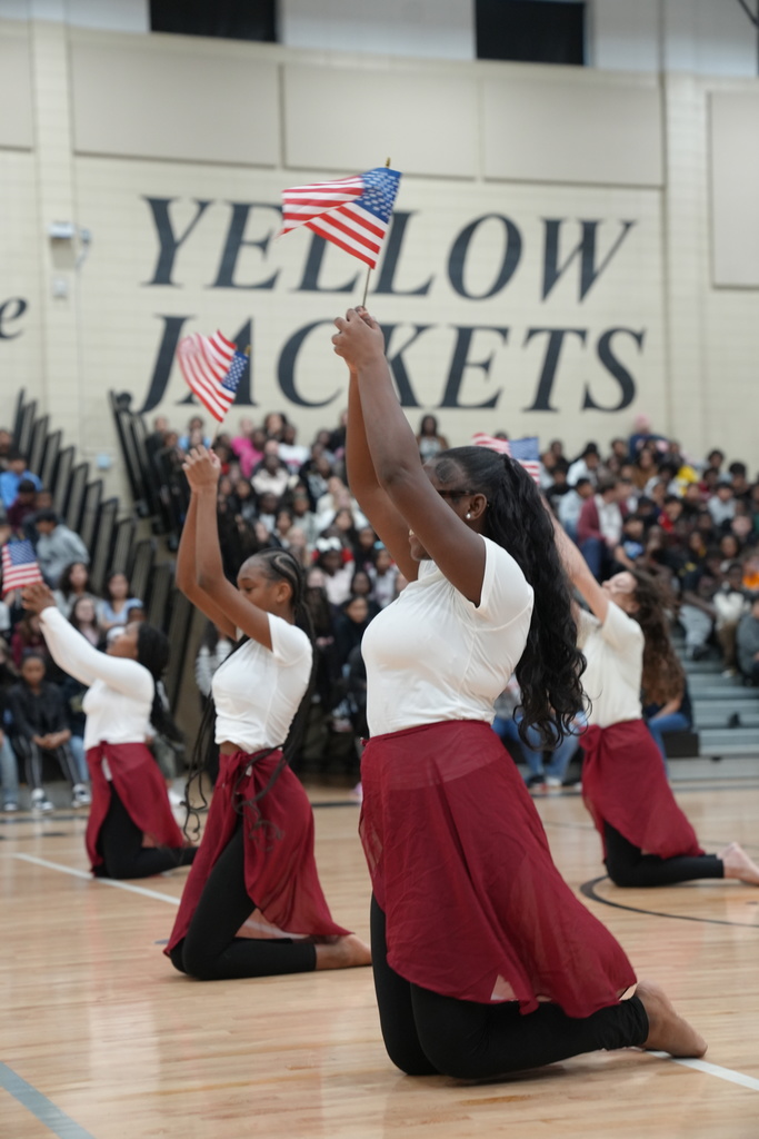 Dancers perform for a crowd inside McAdory Middle School's gym. The dancers kneel on the ground and hold up American flags.