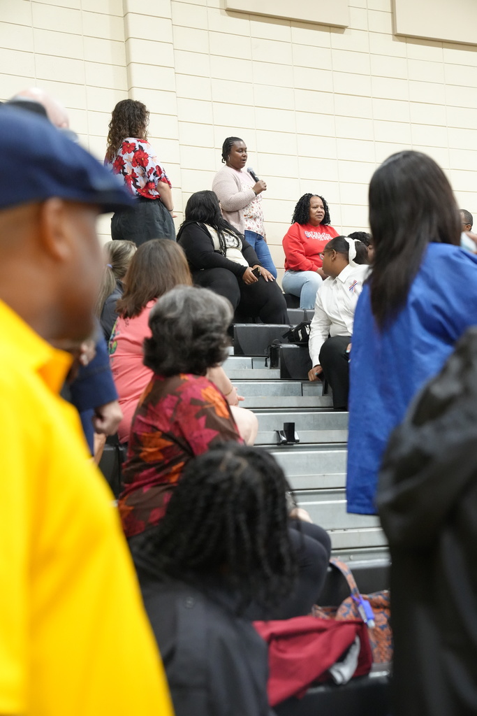 A woman holds a microphone and speaks to a crowd inside McAdory Middle School's gym.