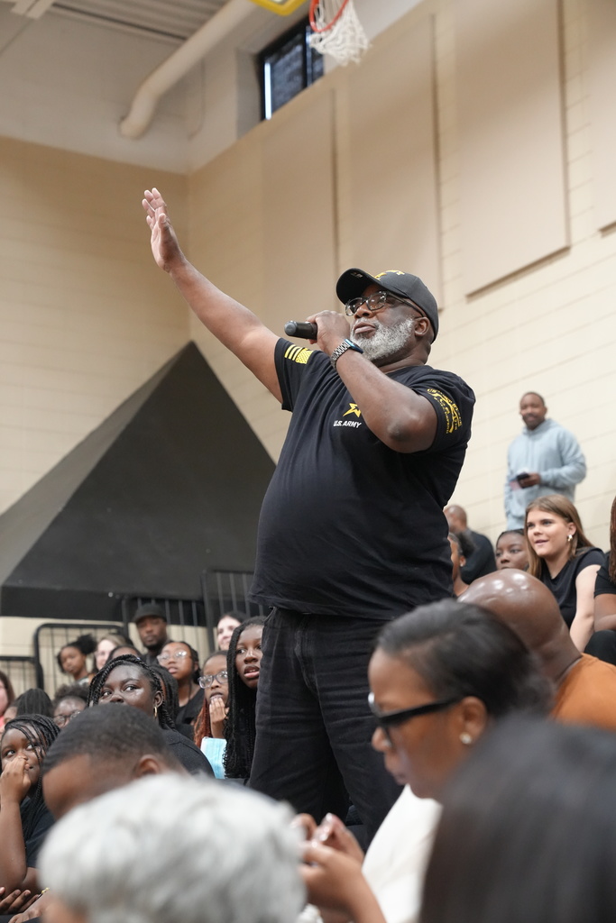 A man wearing a U.S. Army shirt holds a microphone and speaks to a crowd at McAdory Middle School.