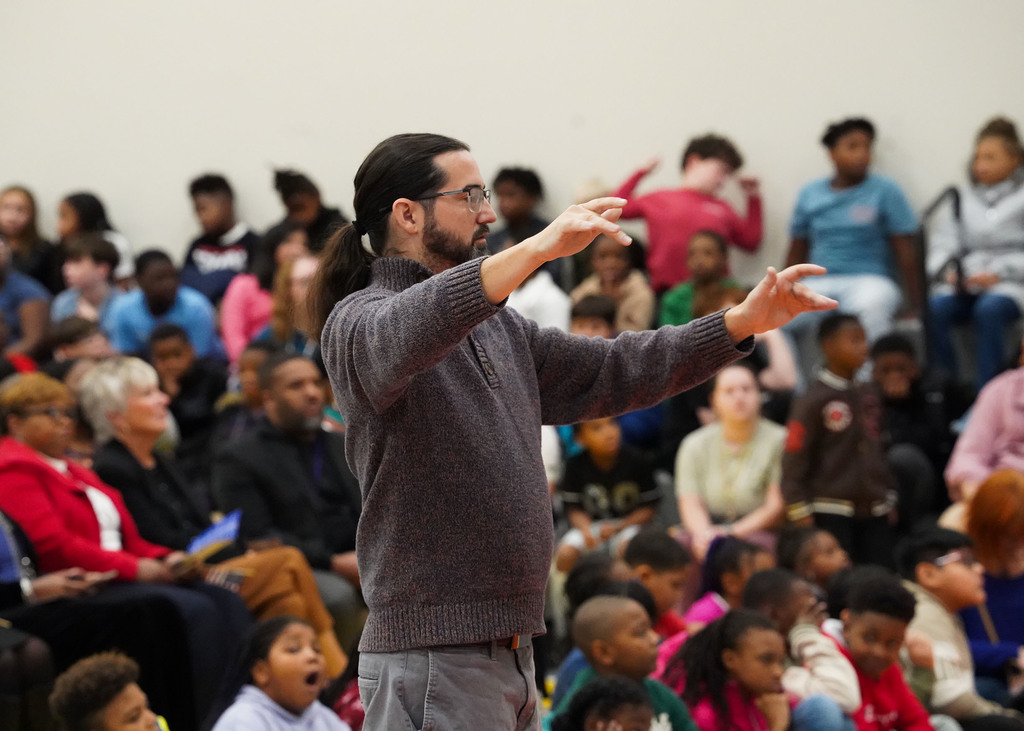 A band director holds up his arms while directing the band. 