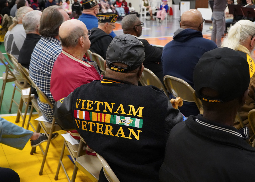 Picture of audience members at a Veterans Day program. The picture features a black jacked that says "Vietnam Veteran" on the back. 