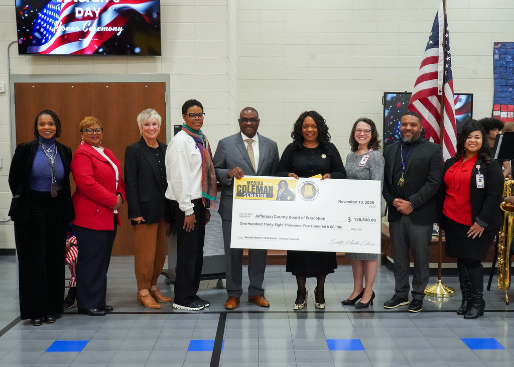 Senator Merika Coleman stands with school leaders and holds a check for the Jefferson County Board of Education in the amount of $138,500.