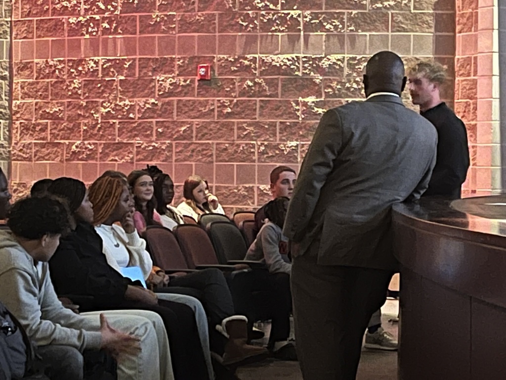 JEFCOED Superintendent Dr. Walter Gonsoulin speaks with a group of middle and high school students during the Superintendent's Student Advisory Council Meeting. They sit and stand in a school auditorium.
