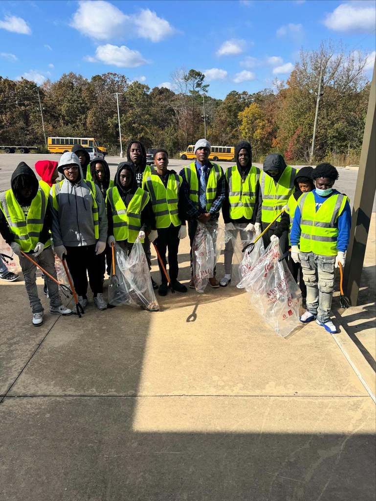 A group of Erwin Middle School basketball players stand together for a photo on a sidewalk. They hold bags of trash and wear yellow work vests.