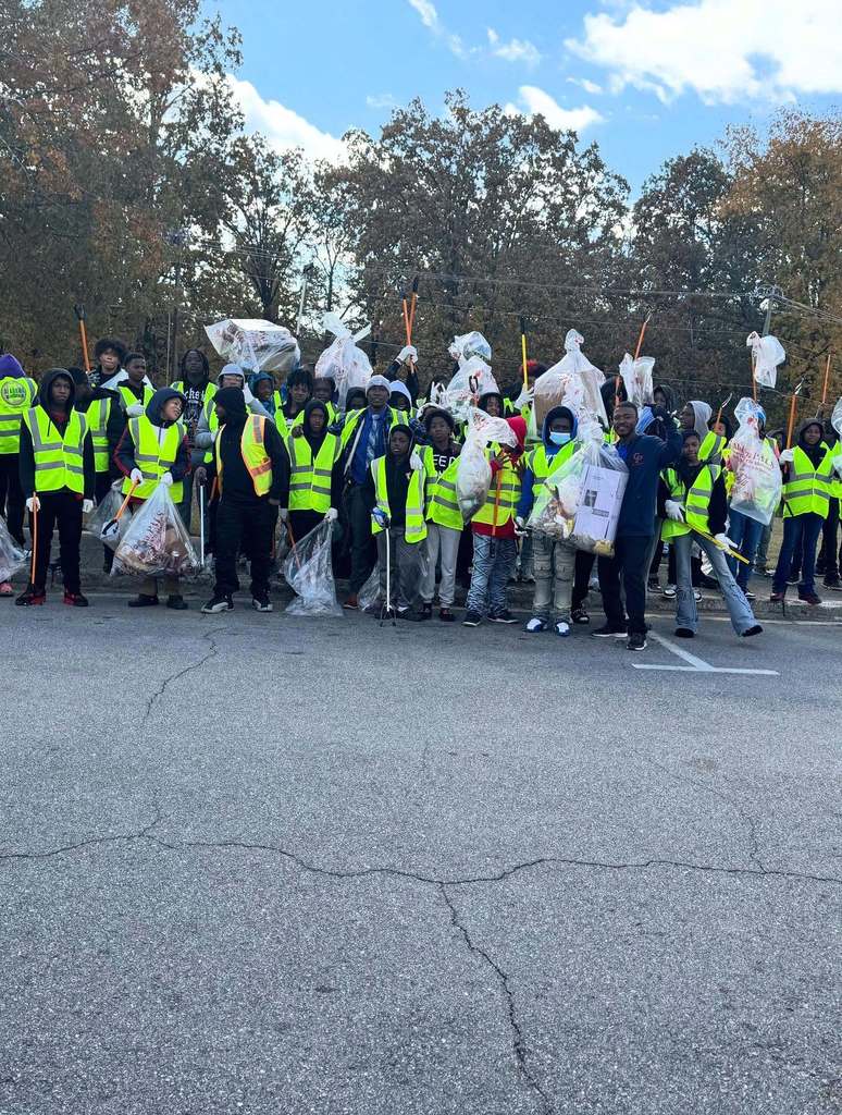 Erwin Middle School basketball players stand together for a photo outside in a parking lot. They hold up bags of trash and wear yellow work vests.