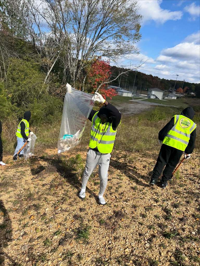 Students wearing yellow vests clean up trash outside a school.