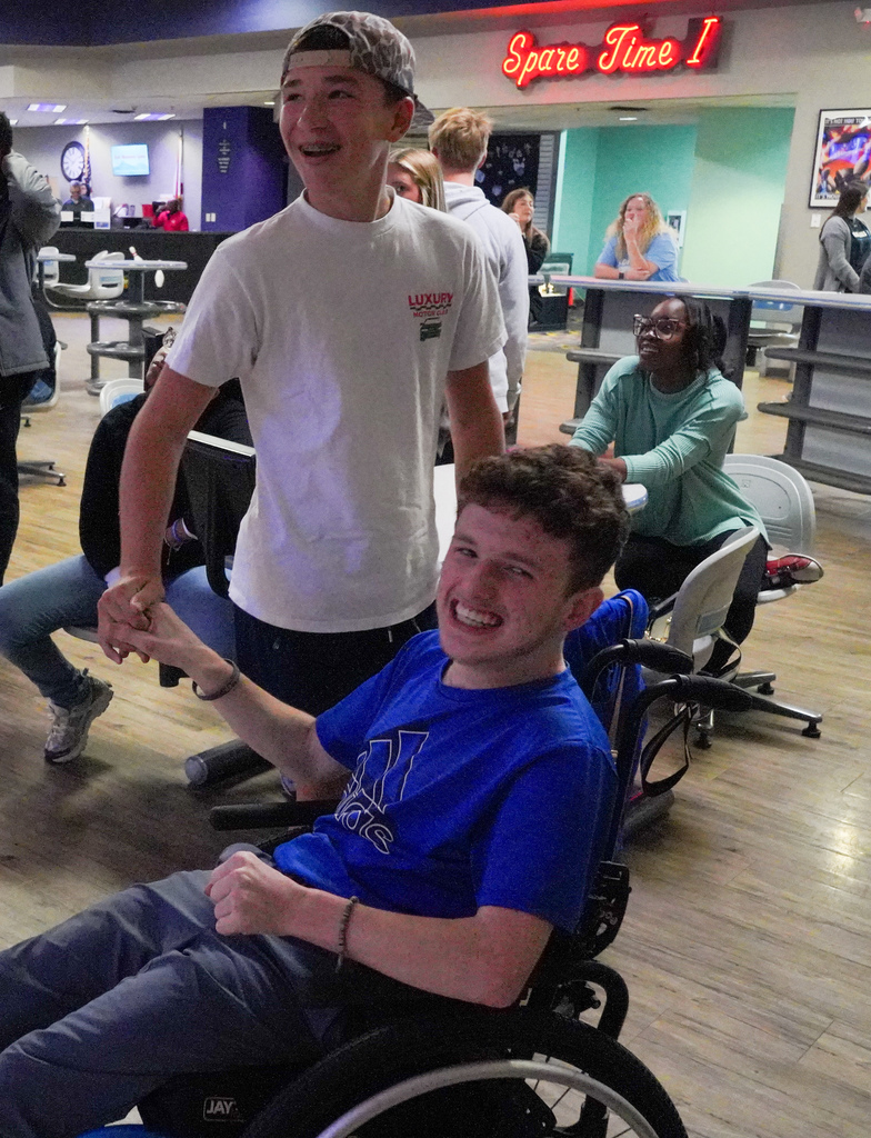 Two students smile and shake hands while bowling at a bowling alley.