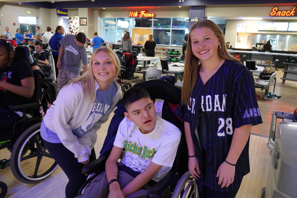 Three students stand and sit together for a photo inside a bowling alley.
