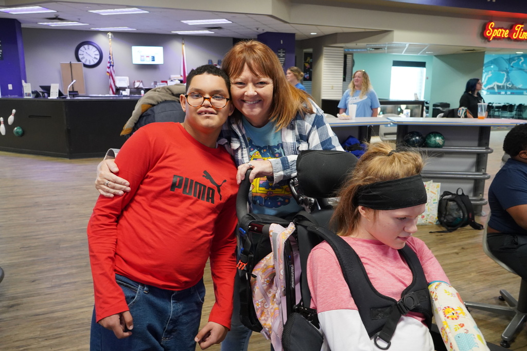 Two students and an adult stand together and smile for a photo at a bowling alley.