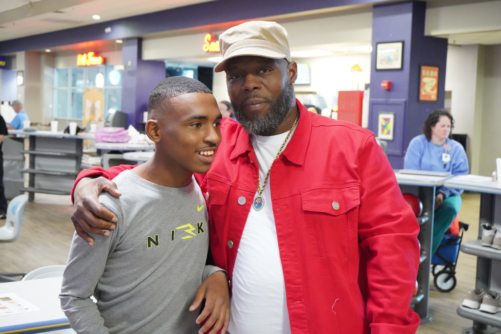 A man and a student stand together for a photo while at a bowling alley.