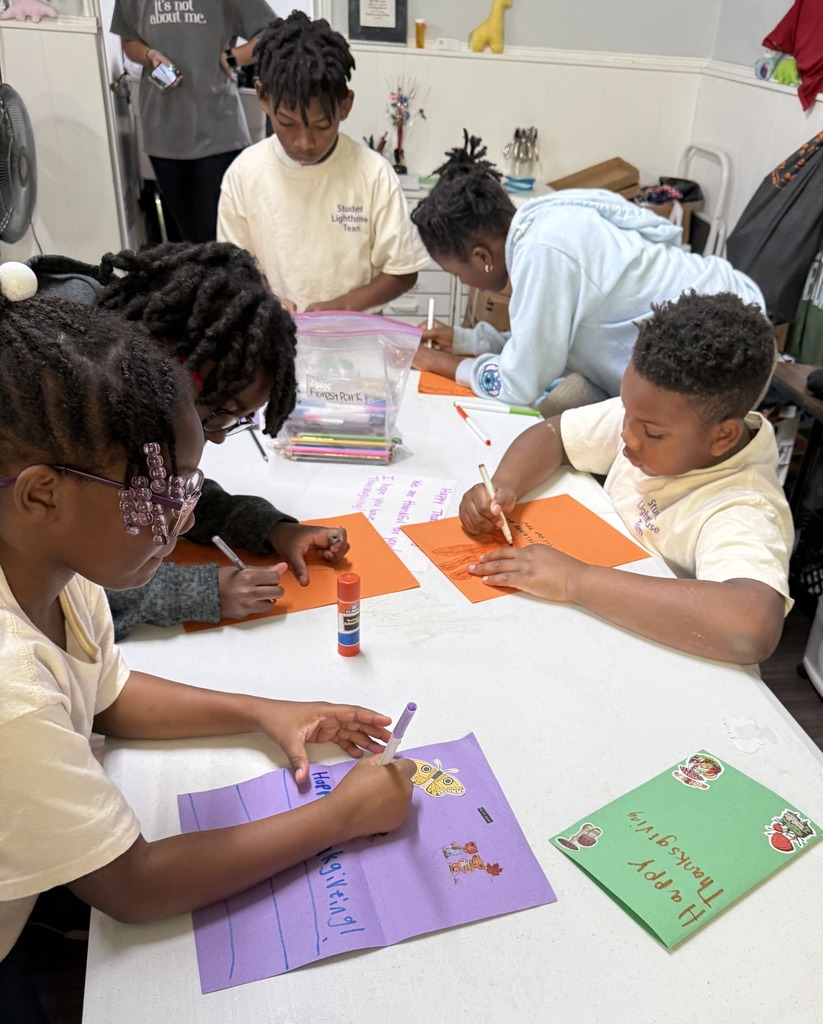 Students sit at a table and write messages on colorful pieces of paper.