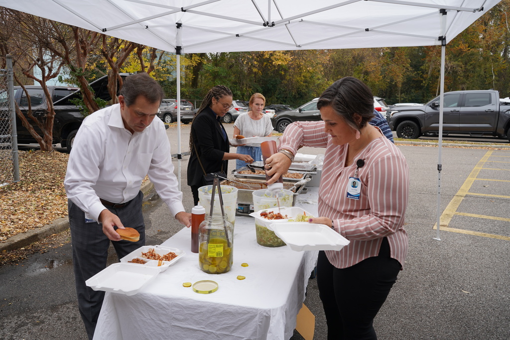 JEFCOED employees fix plates of BBQ and sides while standing under a tent in a parking lot.