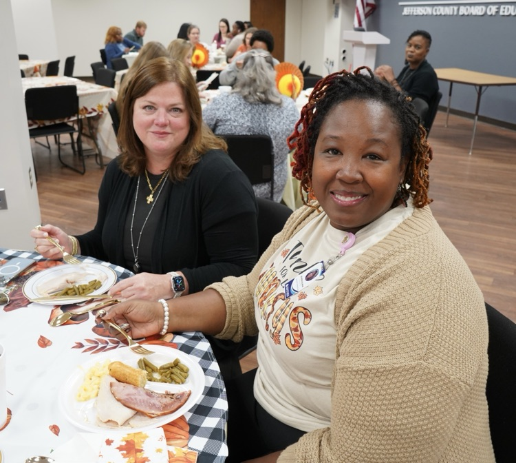 Two women smile while sitting at a table and eating lunch.