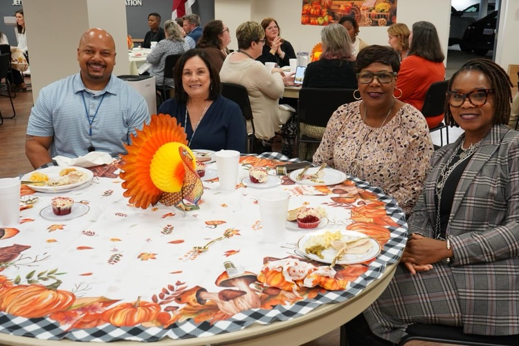 A group of JEFCOED employees sit together at a table and smile while eating a Thanksgiving lunch.