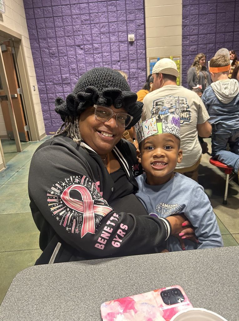 An adult and a child sit together at a school lunchroom table and smile for a photo.