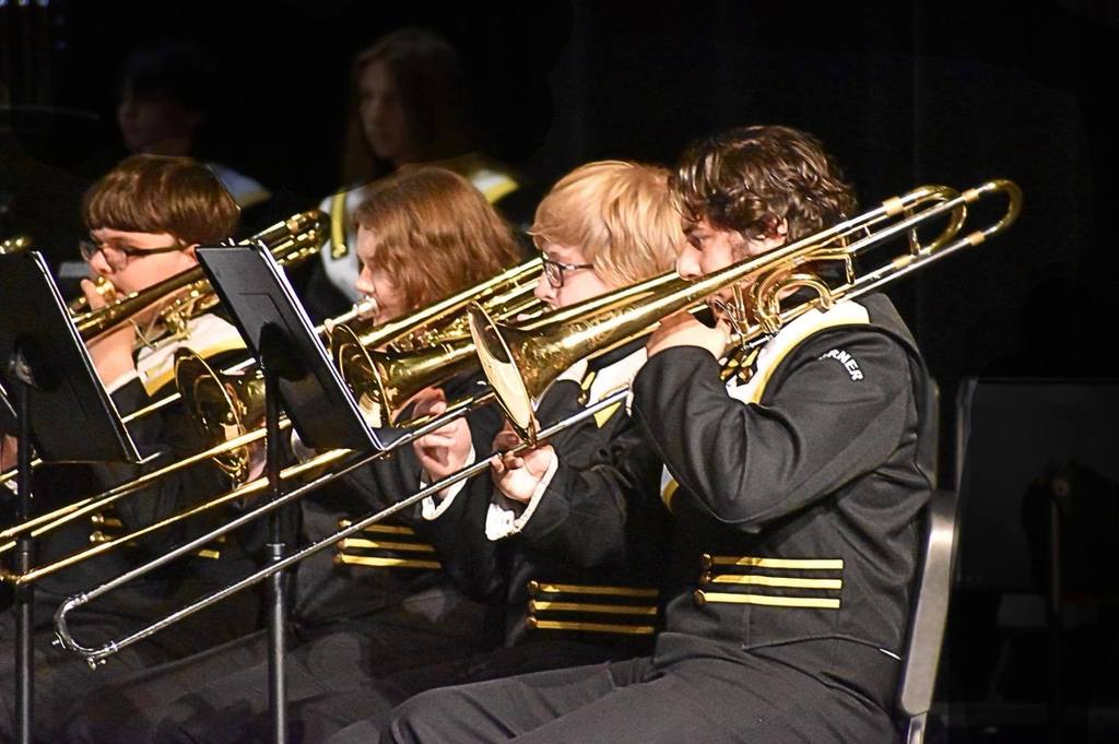 Corner High School students play trombones on a stage.