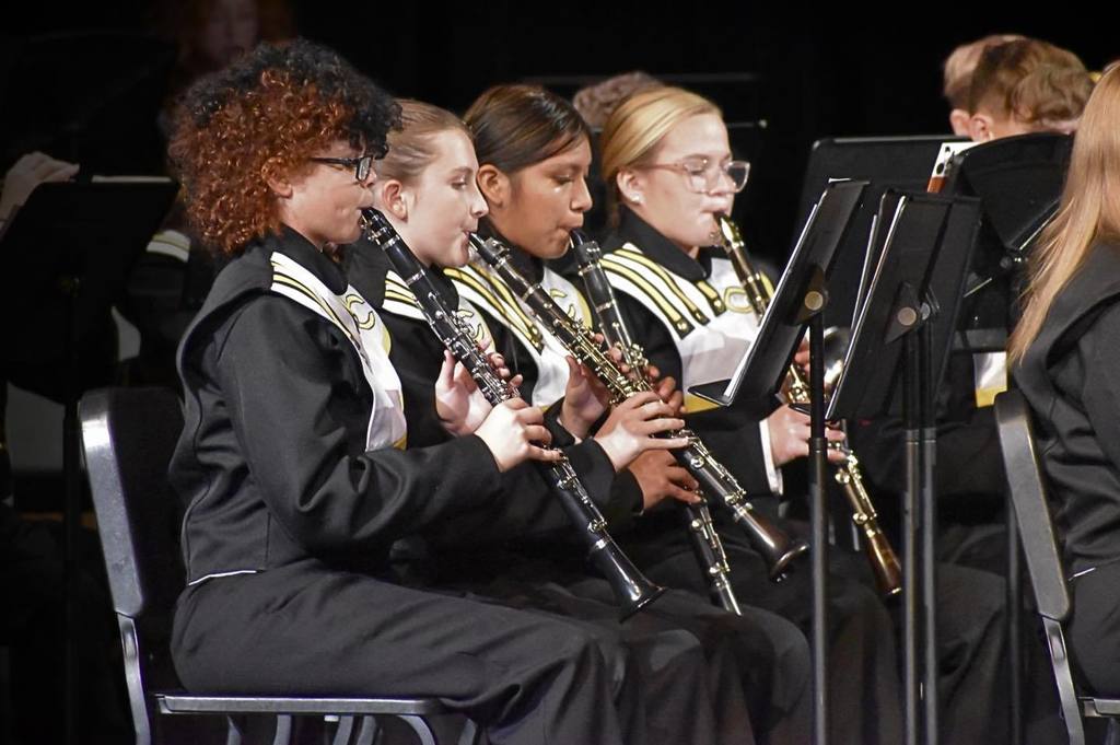 Corner High School students play clarinets on a stage.