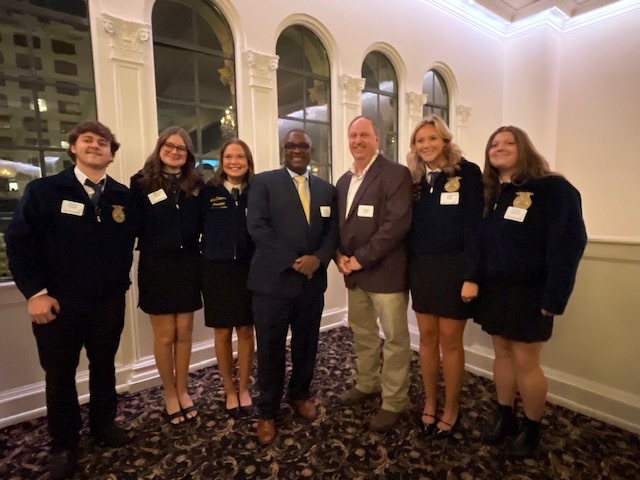 A group of students and an adult stand together in a banquet hall for a photo with JEFCOED Superintendent Dr. Gonsoulin.