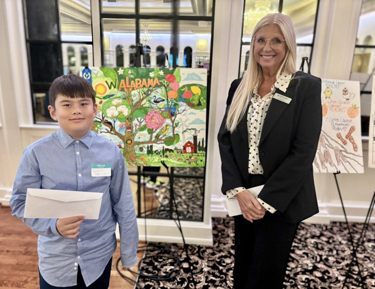 A child and a woman stand together in front of a hand-made poster and smile for a photo.