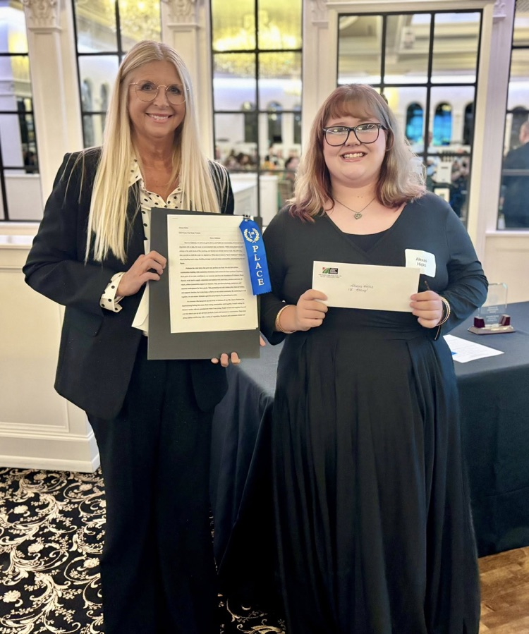 A woman and a student stand together for a photo. They both hold awards in their hands  