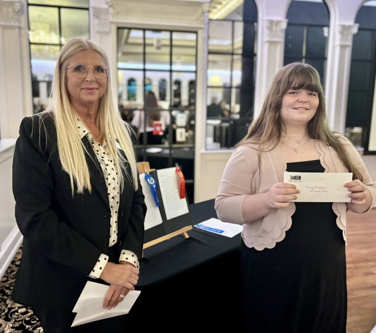 A woman and a student stand together for a photo. They both hold awards in their hands  
