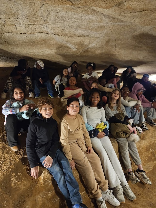 A group of students smile while sitting in a cave.