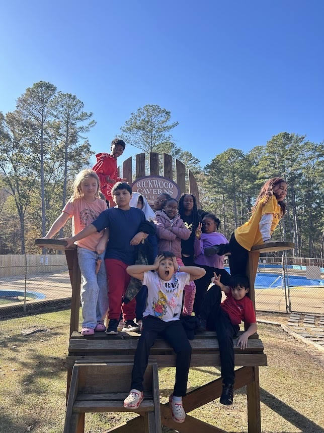 Students pose together for a photo while standing on an oversized chair that says "Rickwood Caverns."