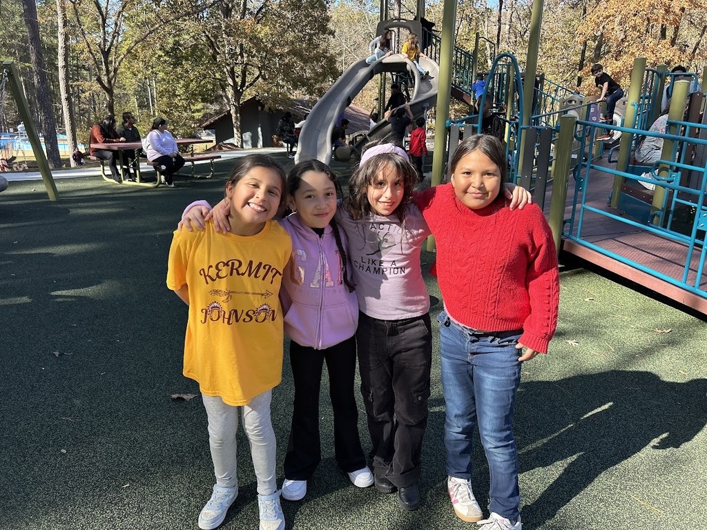 Four students smile and stand together for a photo on a school playground.