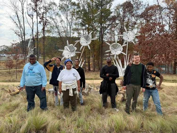 Hueytown students stand in front of sculptures in a green space and smile for a photo.